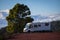 Holiday vacation and travel adventure concept lifestyle. Big motorhome camper van parked near a big tree and blue sky with