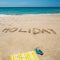 Holiday written on the beach with towel and flip flops over sea