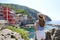 Holidays on Cinque Terre, Italy. Tourist girl looking at village nestled between the rocks overhanging cliffs, Riomaggiore, Italy