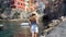 Holidays in Italy. Beautiful woman walking in Riomaggiore harbor looking at quaint village overhanging cliffs, Cinque Terre, Italy