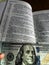 The Holy Bible in English with a tab from the $ 100 banknote showing a passage from the Gospel according to St. Matthew 6:24