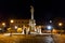 Holy Trinity Column on the Trg Svetog Trojstva Square in the Osijek Fortress, called Tvrdja, by night, with people passing by.