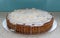 Home baked Bakewell Tart cake on foil platter. Photo shows pastry, white icing and flaked almonds.