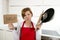 Home cook woman in red apron at domestic kitchen holding pan and household in stress