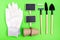 Home gardening. Miniature gardening tools: scoop, rake, inscription board, gloves and chalk on green cardboard