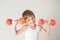 Home indoors leisure activity of young small child in white tank top lifting dumbbells made of red apples during sport fitness