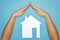 Home insurance concept. Hands in form of roof over house of white paper on blue background