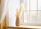 Home interior. Reed plume stem, vase with dry flower on window