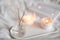 Home liquid fragrance in glass bottle and burning candles staying on white ceramic tray in bed close up.