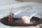 Home liquid fragrance in glass bottle with wooden sticks and scent candle with open paper book on tray in bed