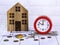 Home loan concept. Wooden house, red alarm clock, house keys, coins, stationeryGenerated image