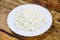 Home made fresh large cottage cheese on white plate on wooden background. Top view.