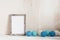 Home minimal decor. Portrait empty wooden frame mockup with blue balls garland. Nice and cozy composition. White wood table and