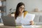 Home office. Concentrated arab businesswoman working with papers and laptop, holding cup with hot beverage