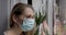 home quarantine - woman with medical face mask looking through window and waving with hand to friend