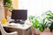 Home real working place with table, turned off computer, green house plants, yellow cup and notepad near window.