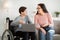 Home schooling. Cheerful disabled teen boy in wheelchair holding laptop, talking to his mom or teacher indoors