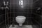 Home toilet room, walls covered with black tiles, bidet and toilet with open lid, modern interior design, plumbing.