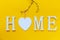 Home, wooden text with heart shape decor on yellow background. Concept of building houses, choosing your own house, mortgage,