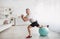 Home workout. Senior man doing lunges with fitball, exercising at home and smiling at camera, copy space