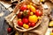 Homegrown assorted red, yellow, orange tomatoes in wicker straw basket stands on sackcloth on rustic wooden table