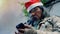 A homeless elderly Asian man wearing red christmas hat stands next to wall using his mobile phone to seek work and government