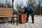 homeless elderly old Caucasian man rummages for food and garbage in trash can in a park in autumn