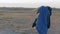 Homeless little girl stands in a field. Covers his head with a blanket and plays on the territory of the refugee camp