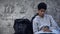 Homeless male teen sitting at street near backpack, poverty problem, refugee