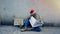 A homeless man, an old Asian man wearing a red Christmas hat, is sitting on the ground reading a newspaper, Look for jobs from