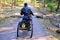 A homeless man in a wheelchair rides on a forest road. The three-wheeled wheelchair is equipped with a box for things. Silhouette
