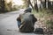 A homeless person covers his face and wears a torn hat. Ragged, dirty, sitting on the side of the road in the capital