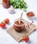 Homemade adjika sauce is an appetizer with tomatoes and hot peppers in a jar on a light background with fresh herbs and vegetables