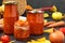 Homemade adzhika with tomatoes, apples and carrots in jars on a dark background