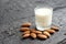 Homemade almonds milk in a clear glass and pile of roasted almonds on black wooden plank