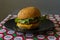 Homemade appetizing cheeseburger with melted cheese in a toasted bun with sesame on a red tablecloth on a gray background.