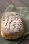 Homemade artisan sourdough bread loaf with artistic leaf pattern scoring and a wavy line in the middle on a green kitchen towel