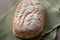 Homemade artisan sourdough bread loaf with artistic leaf pattern scoring and a wavy line in the middle on a green kitchen towel