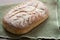 Homemade artisan sourdough bread loaf with artistic leaf pattern scoring and a wavy line in the middle on a green kitchen towel