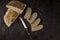 Homemade bread, simple and healthy nutrition. The loaf of bread cut with various slices and a knife, seen from above on a black ba