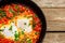 Homemade breakfast shakshuka - fried eggs, onion, bell pepper, tomatoes and parsley in cast-iron frying pan on rustic wooden table