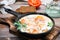 Homemade breakfast of shakshuka fried eggs with tomatoes and herbs in a pan on a cutting board