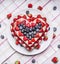 Homemade cake with Strawberries and blueberries for Valentine\'s Day heart shaped on a white plate on a striped tablecloth with sca