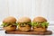 Homemade cheeseburgers on rustic wooden board on a white wooden surface, side view. Close-up