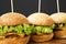 Homemade cheeseburgers on wooden board against black background, side view