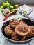 Homemade chicken roasted cutlets in black cast-iron pan on wooden background and raw vegetables