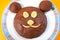 Homemade chocolate cake with eyes, nose and mouth made from banana. Smiling face of brown bear. Chocolate cupcakes on plate in