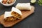 Homemade chorizo breakfast burritos on a rustic wooden board on a black surface, side view
