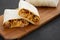 Homemade chorizo breakfast burritos on a rustic wooden board on a black surface, side view. Close-up