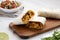 Homemade chorizo breakfast burritos on a rustic wooden board on a white wooden surface, low angle view. Close-up